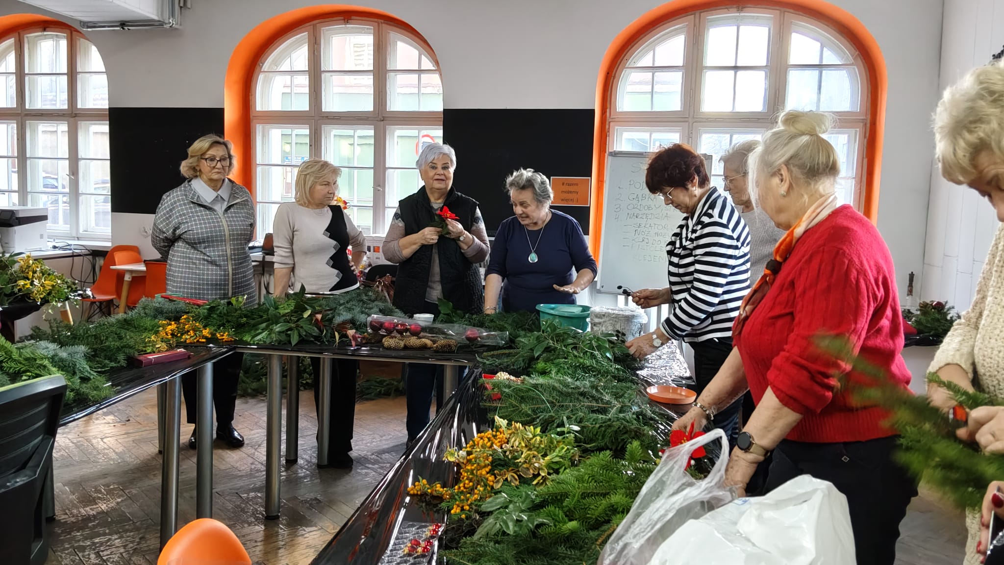 Grupa kobiet stoi przy stole na którym leży dużo gałązek igliwia.
