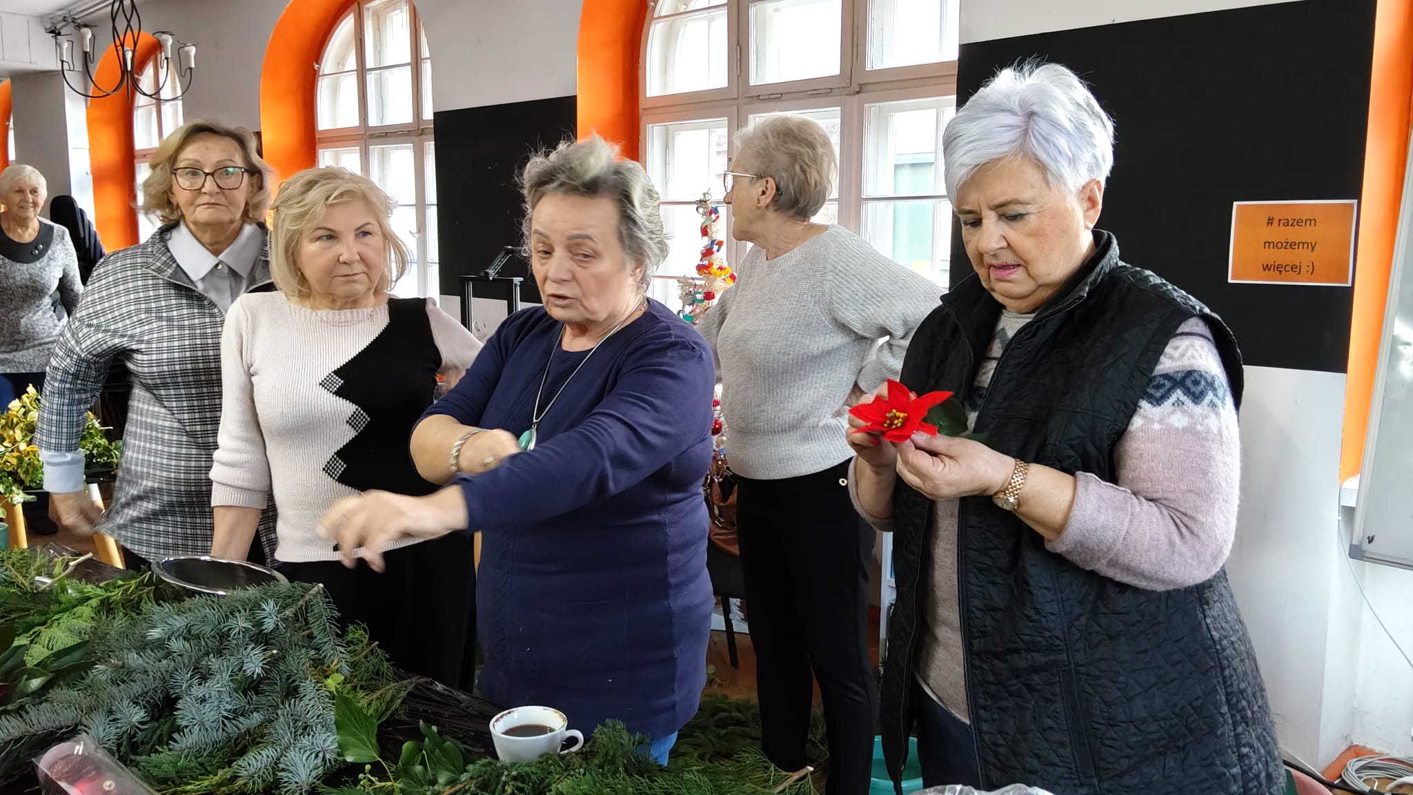 Grupa kobiet stoi przy stole na którym leży dużo gałązek igliwia.