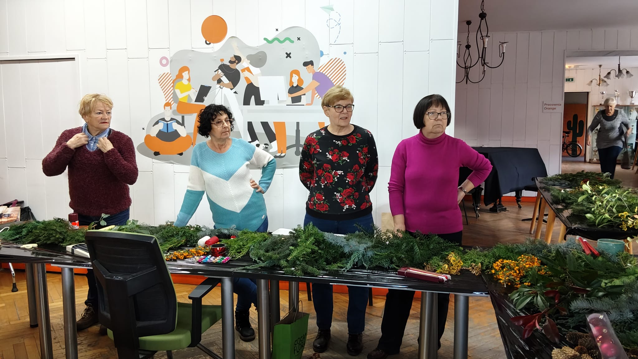 Trzy kobiety stoją przy stole na którym leży dużo gałązek igliwia.