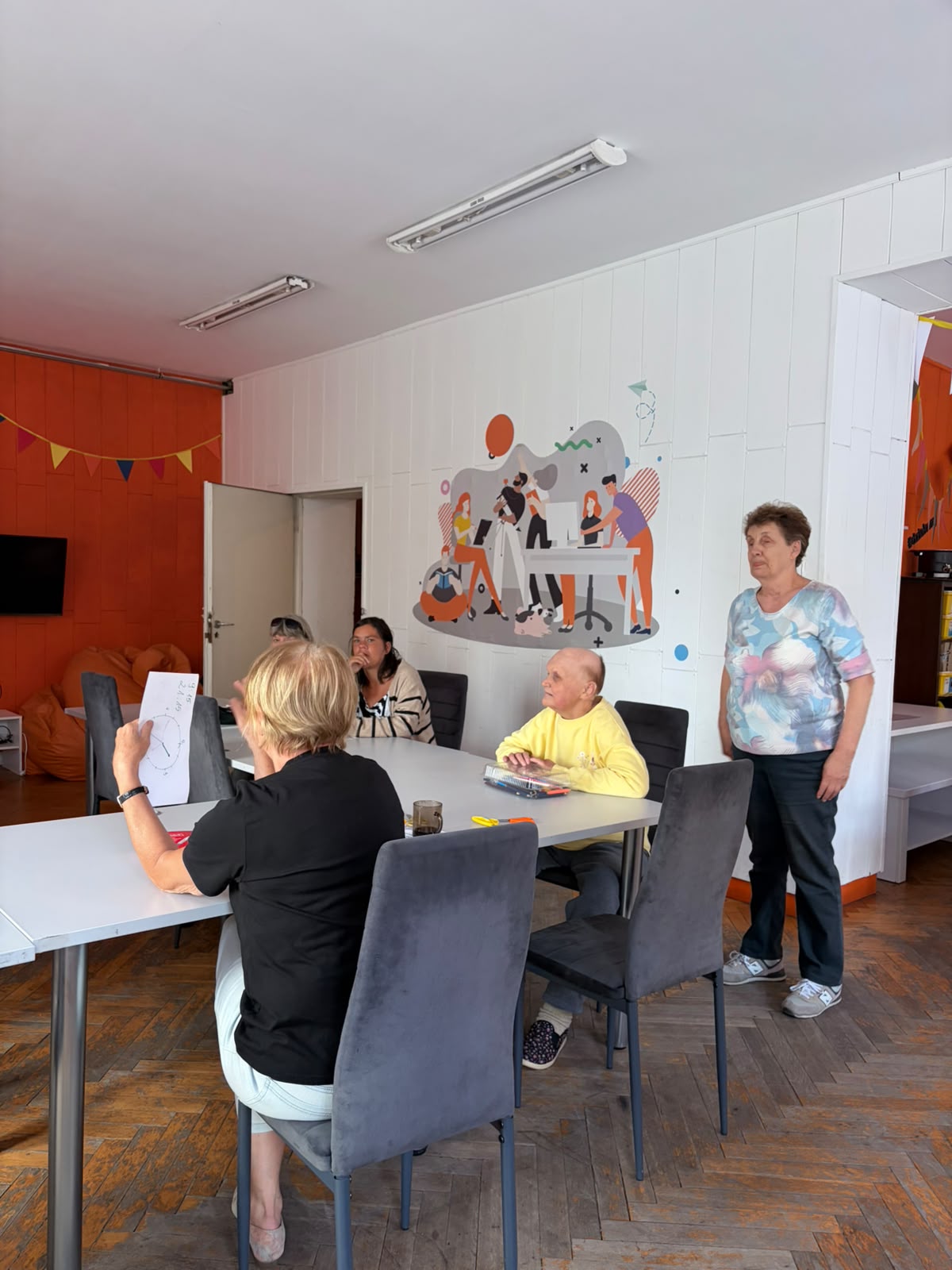 Grupa osób w Pracowni Orange, część siedzi przy stole, część stoi.