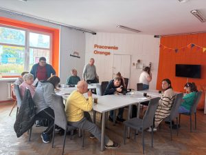 Grupa osób w Pracowni Orange, część siedzi przy stole, część stoi.
