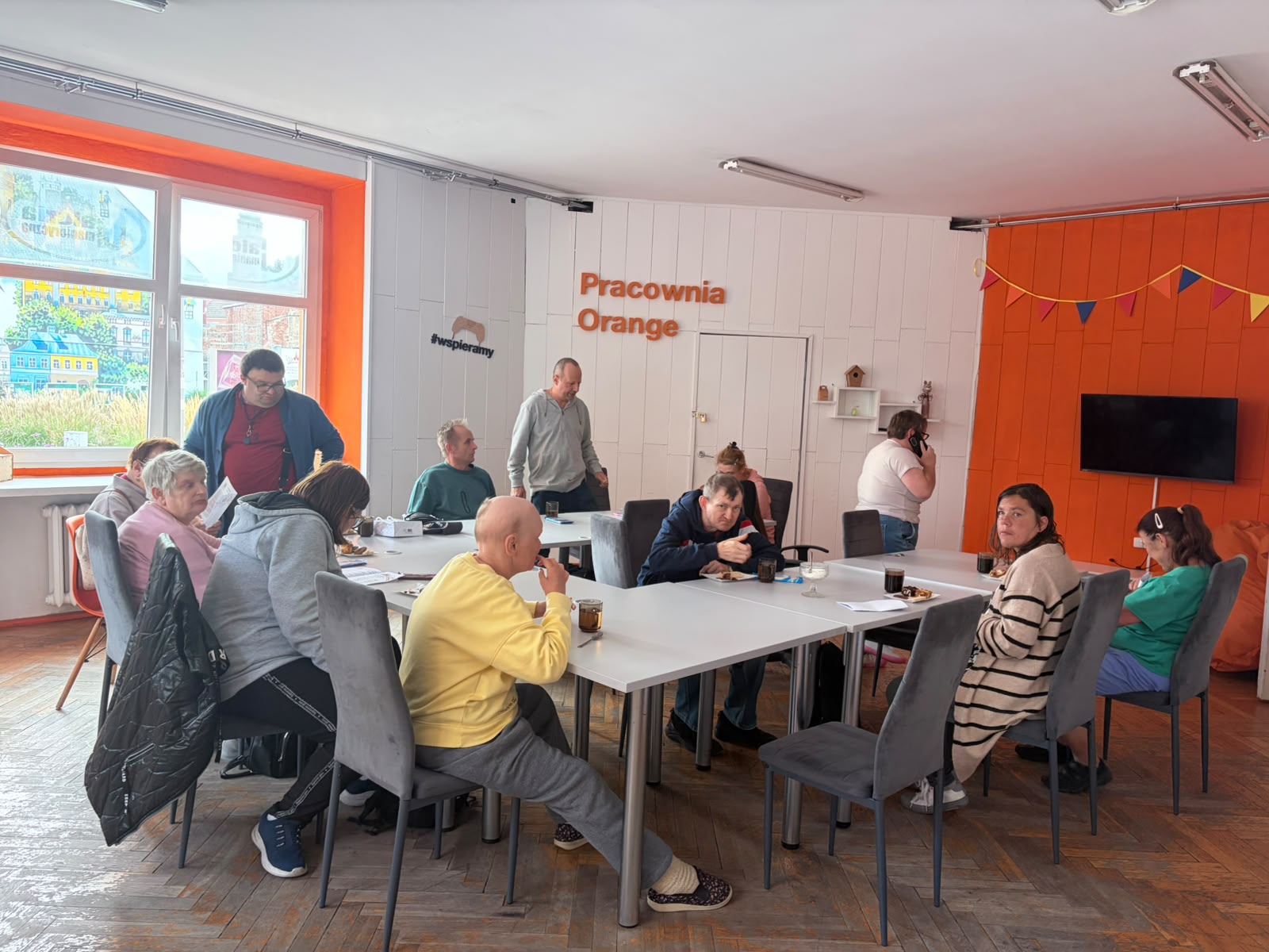Grupa osób w Pracowni Orange, część siedzi przy stole, część stoi.