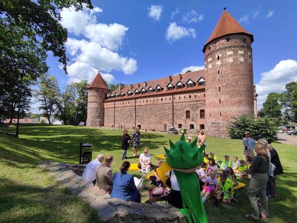 Grupa osób siedząca na trawie, w oddali zamek.