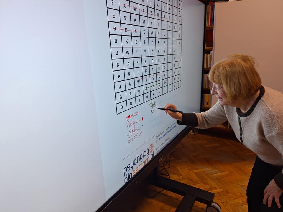Kobieta rozwiązująca zadania na tablicy multimedialnej.