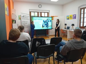 Zdjęcie dwóch kobiet stojących obok ekranu z wyświetloną prezentacją.