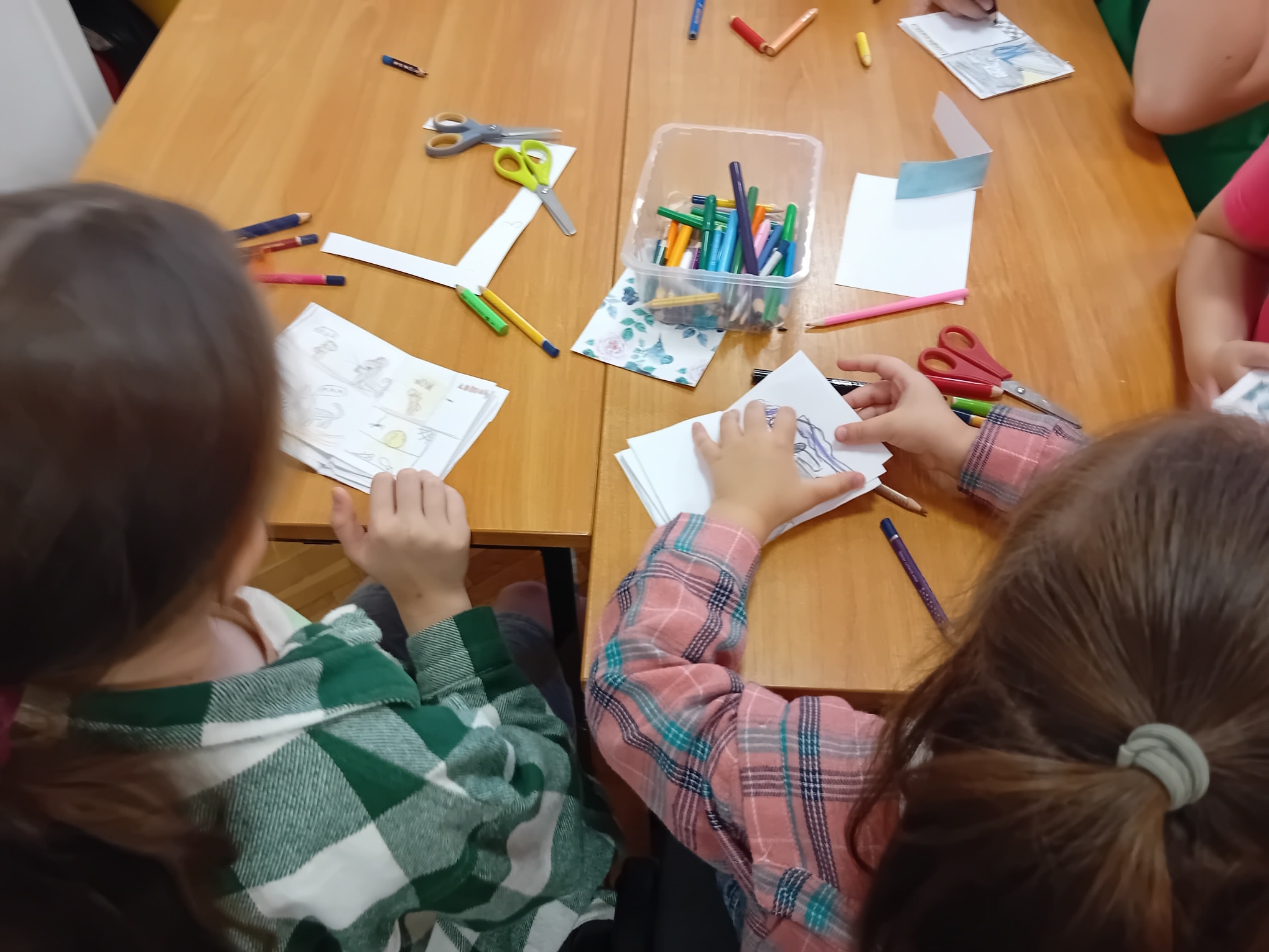 Dzieci siedzą przy stole i rysują.