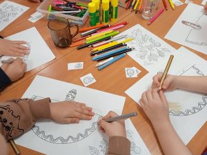 stół z pracami plastycznymi, kredkami, kadr na ręce malujących dzieci