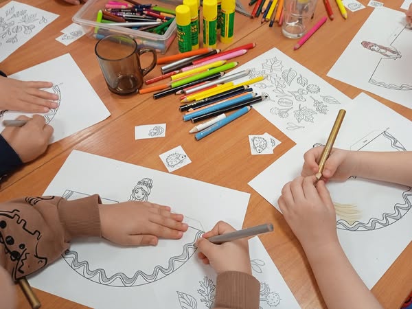 stół z pracami plastycznymi, kredkami, kadr na ręce malujących dzieci