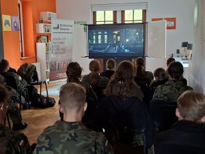 Grupa dzieci ogląda film na ekranie ustawionym w centralnym punkcie.