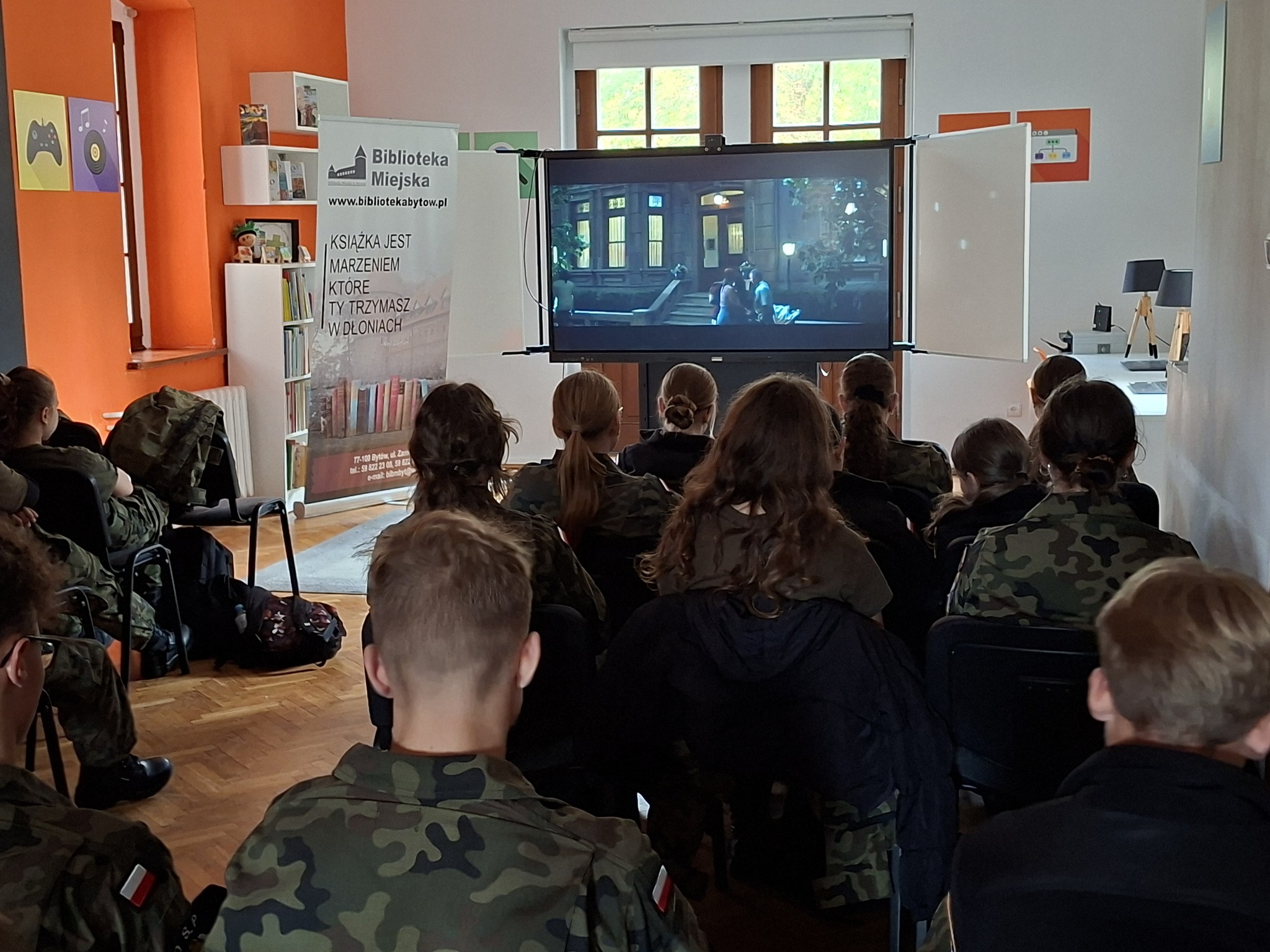 Grupa dzieci ogląda film na ekranie ustawionym w centralnym punkcie.