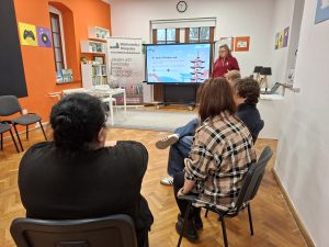 Grupa osób siedzących na krzesłach, przed nimi opowiadająca o mandze kobieta.