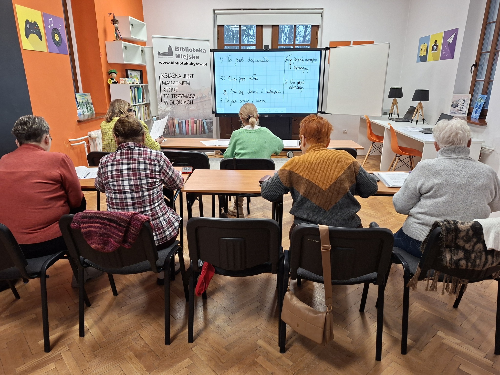 Grupa osób siedząca przed ekranem z wyświetlonymi na nim hasłami.