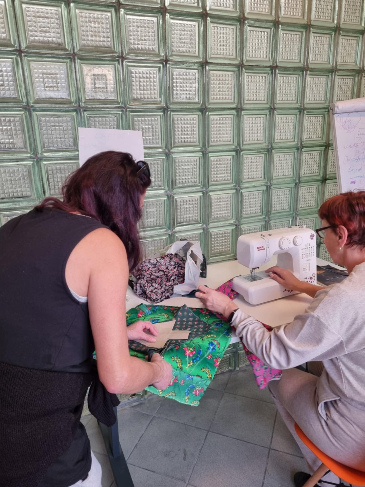 Kobieta w czarnej koszulce wycina choinki z materiału a druga kobieta szyje je na maszynie.
