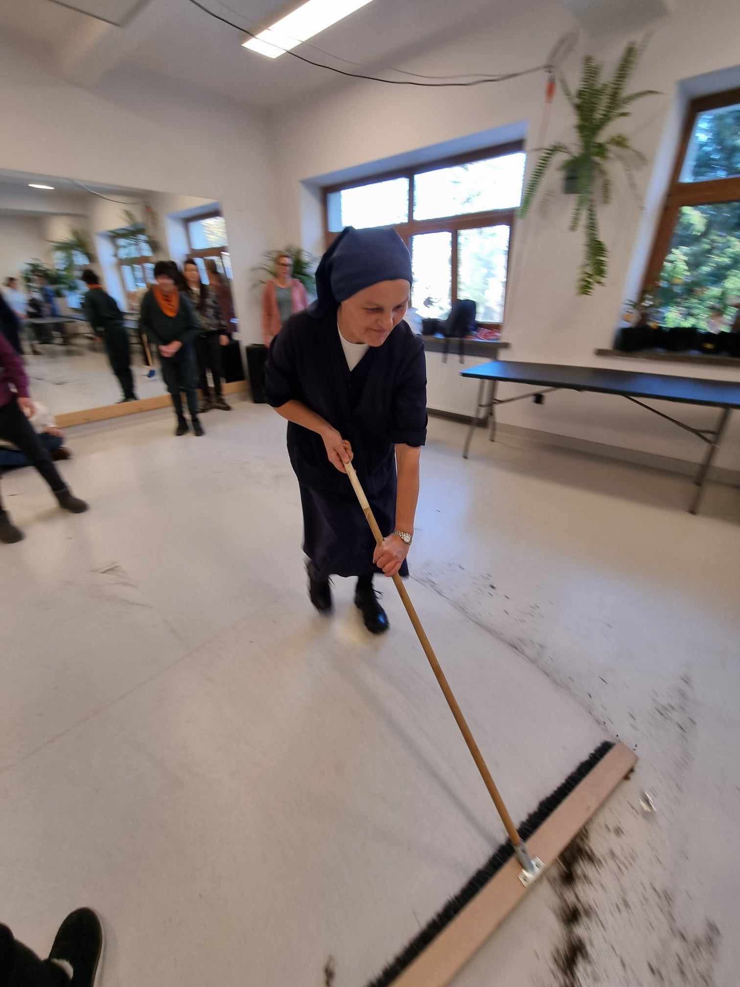 Siostra zakonna zamiata sprząta podłogę, na której jest rozsypana ziemia.