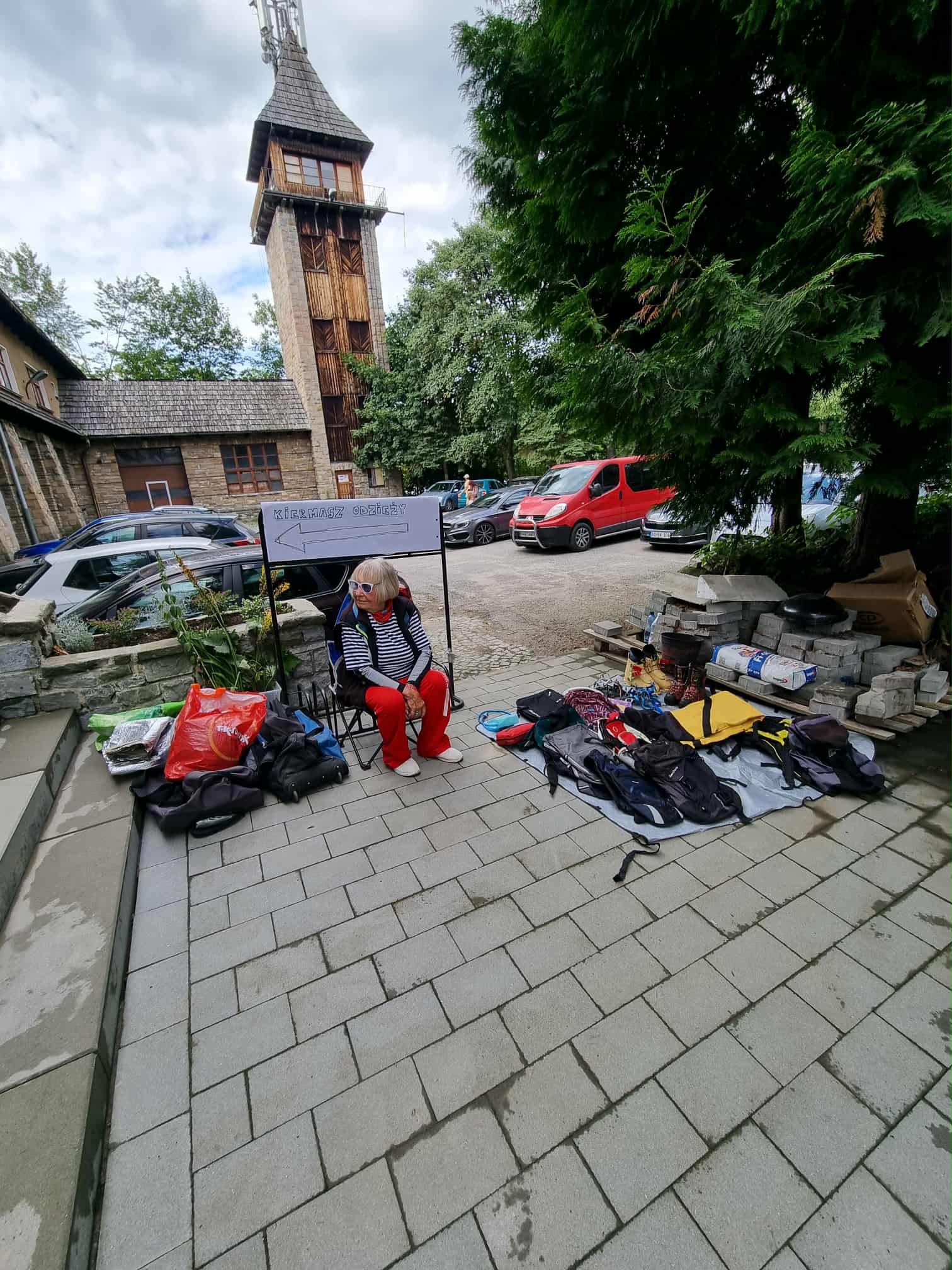 Starsza kobieta siedzi obok rzeczy, które przyniosła na targi.