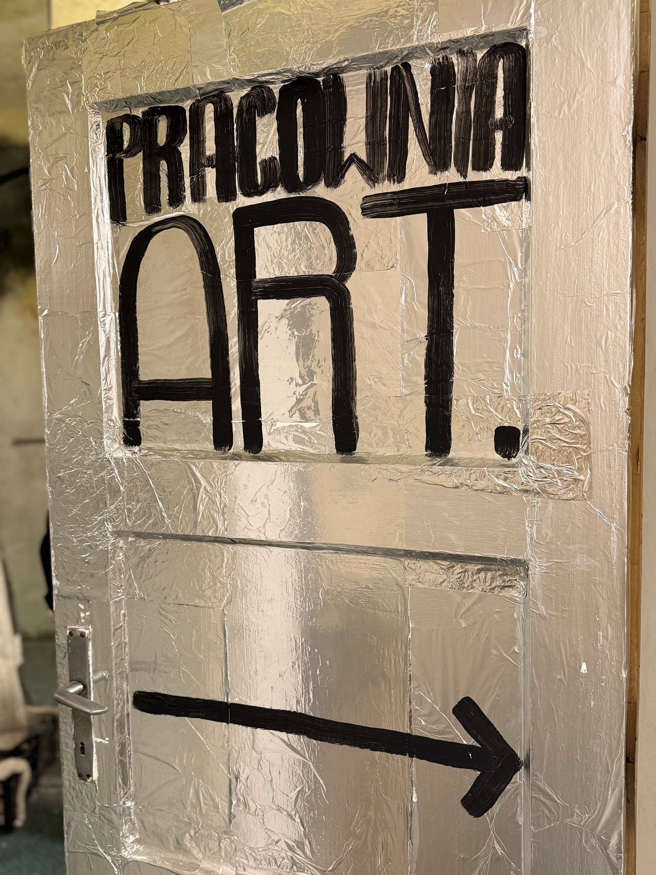 Drzwi pokryte srebrną folią i czarnym napisem Pracownia ART.