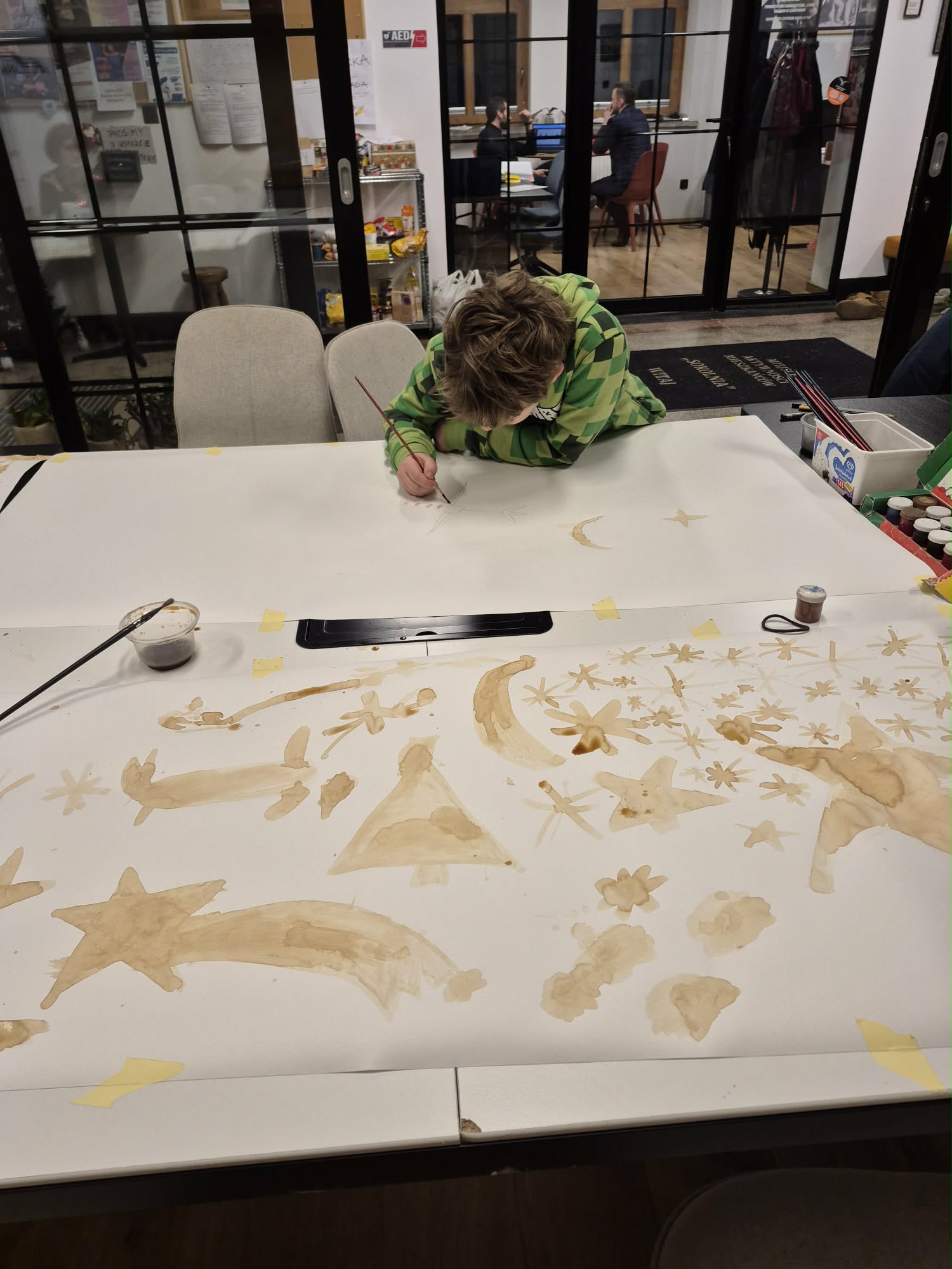 Chłopak maluje kawą świąteczny obrazek.