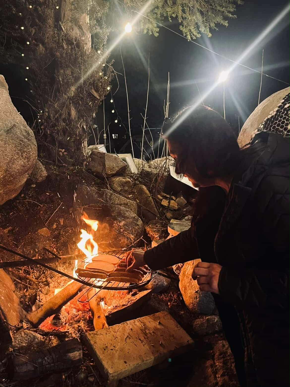 Kobieta smaży kiełbasę w ognisku.