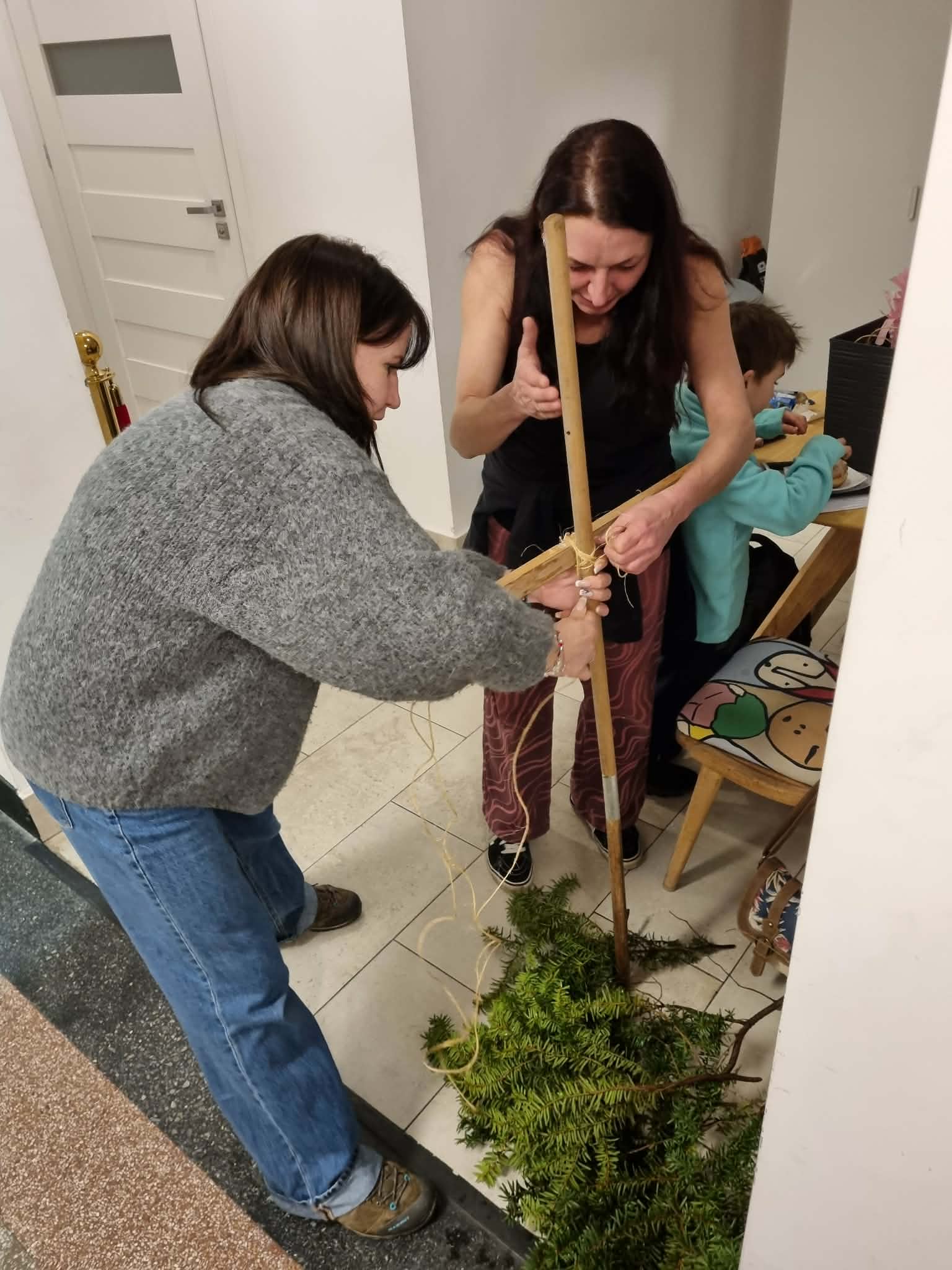 Dwie kobiety związują patyki sznurkiem.