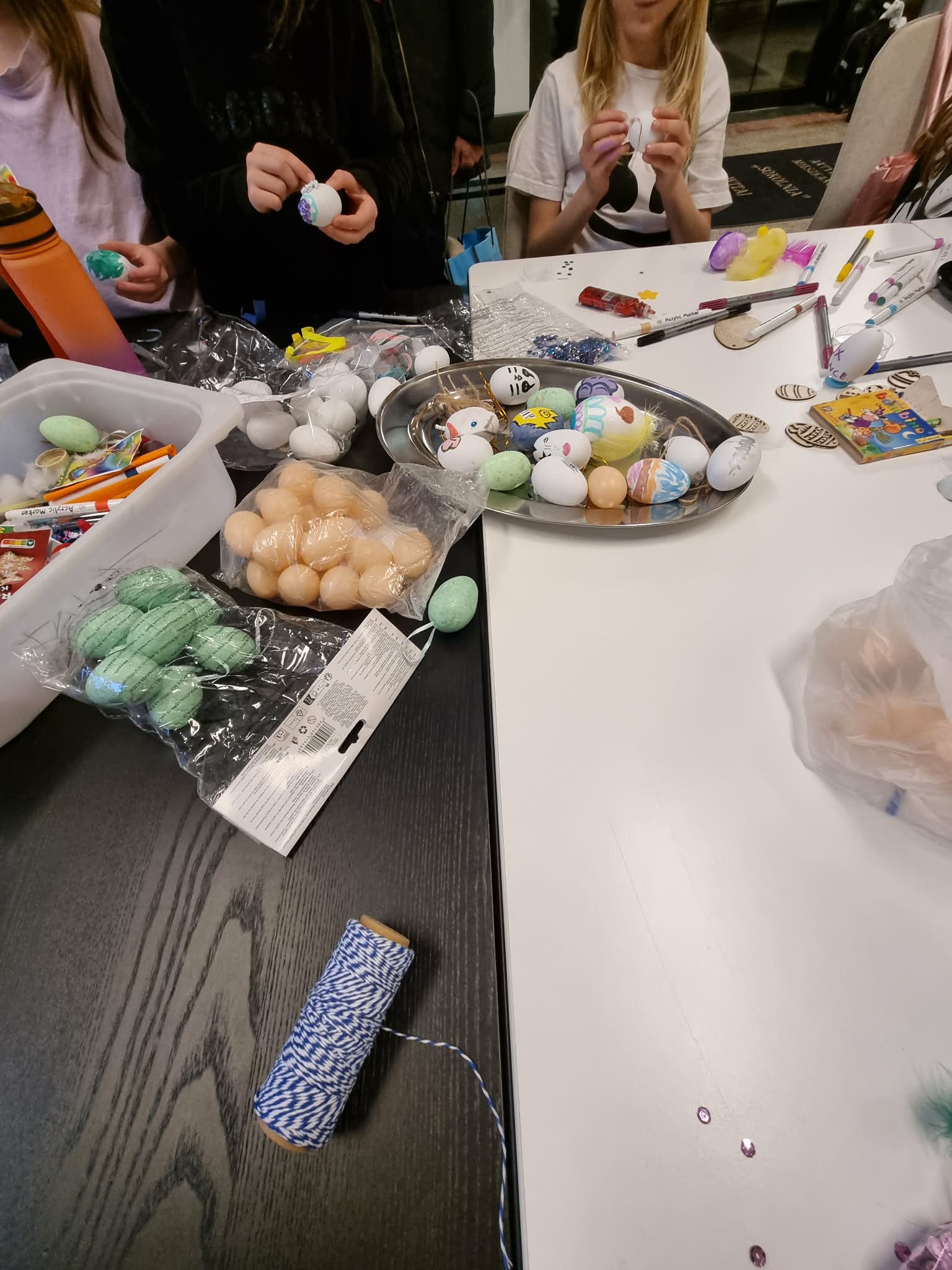 Kilka osób ozdabia różnokolorowe, styropianowe jajka