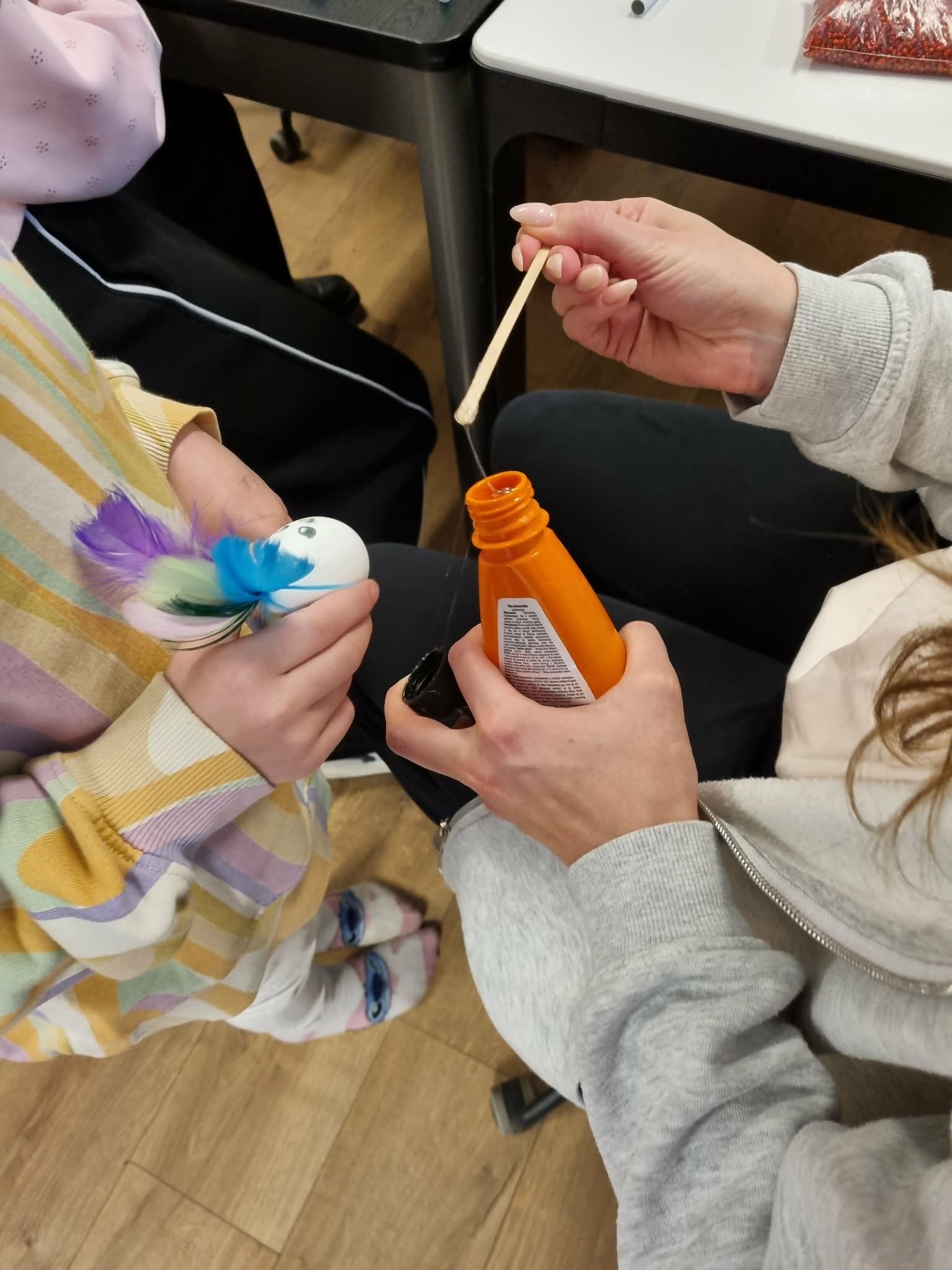 Dwie osoby przyklejają piórka do styropianowych jajek