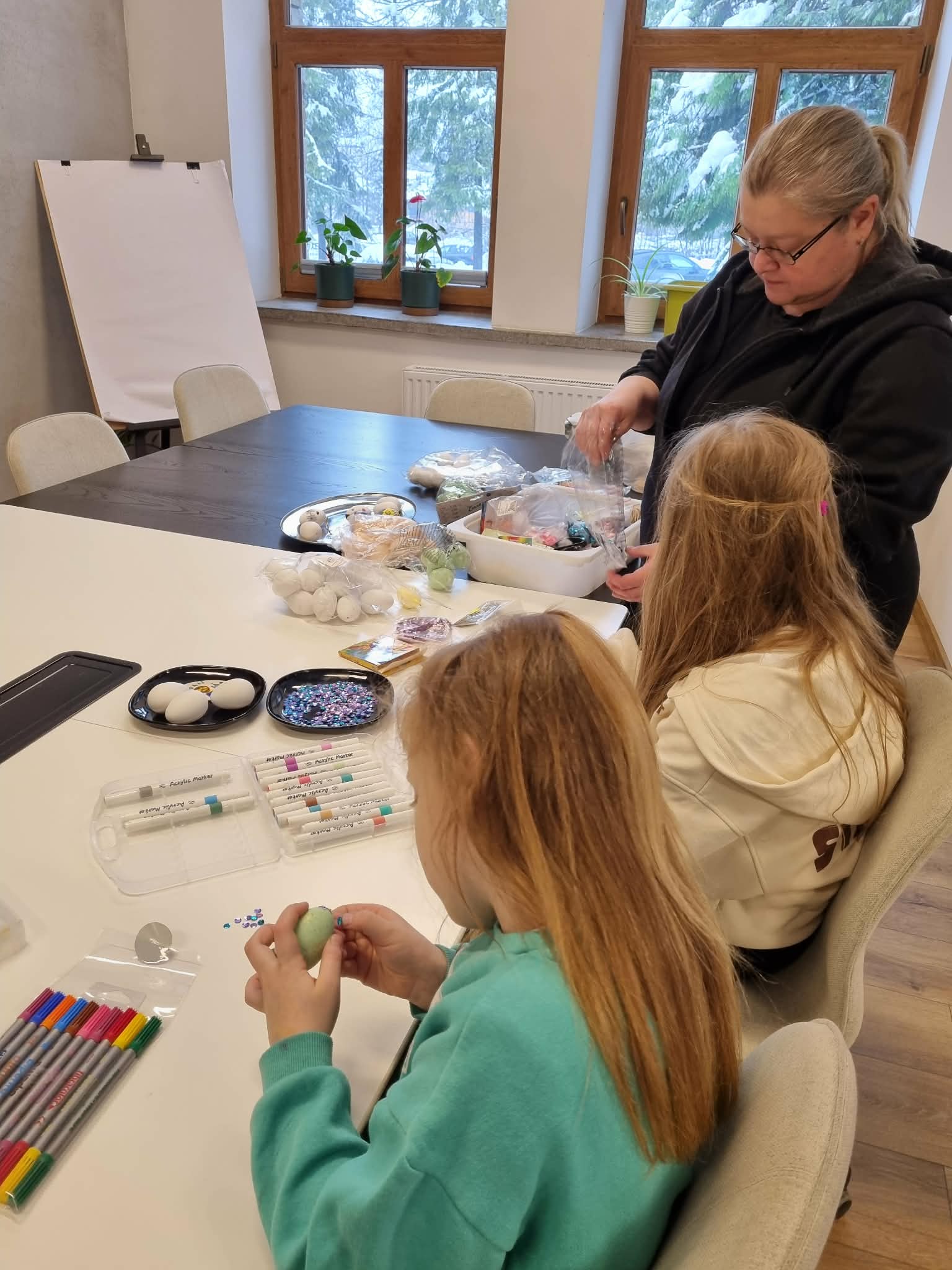 Kobieta i dwie dziewczynki ozdabiają pisanki.