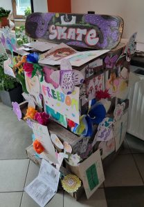 Totem ozdobiony różnymi rysunkami a na szczycie ręcznie malowana deskorolka