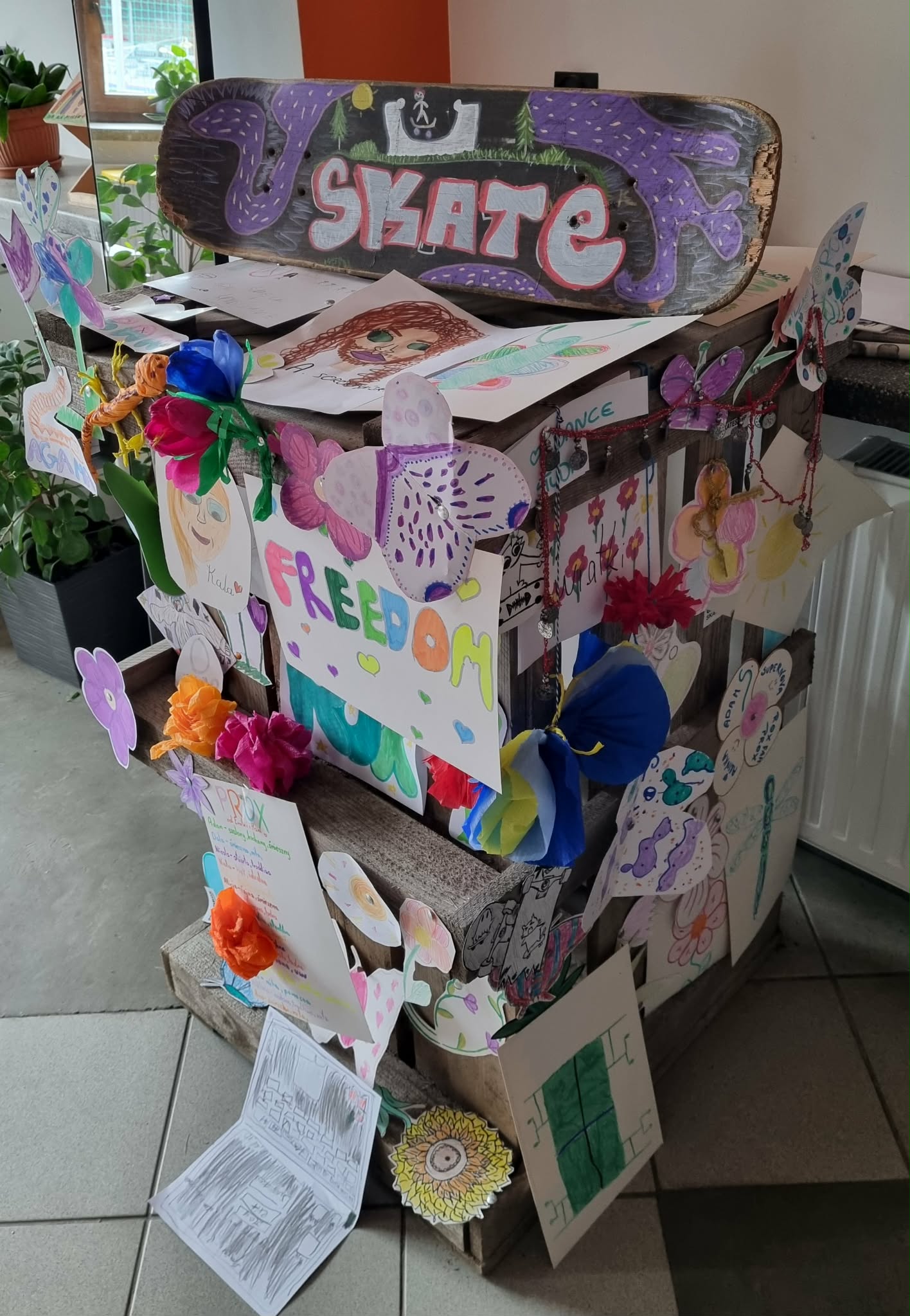 Totem ozdobiony różnymi rysunkami a na szczycie ręcznie malowana deskorolka