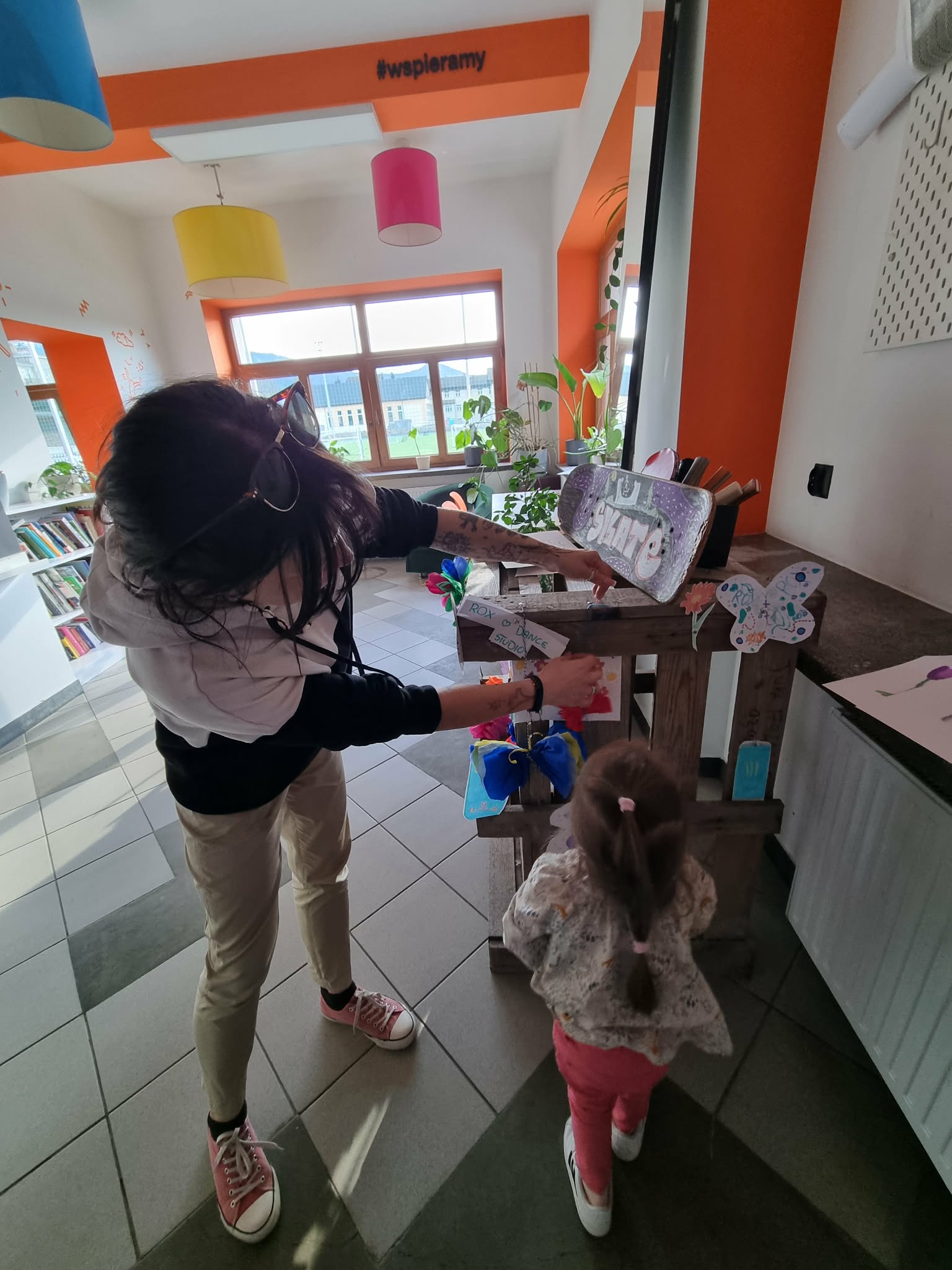 Kobieta z dziewczynką przyczepia swoją ozdobę do drewnianej skrzyni