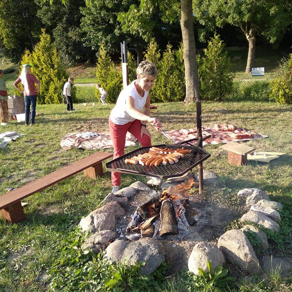 Kobieta pilnująca kiełbasek na grillu nad ogniskiem.