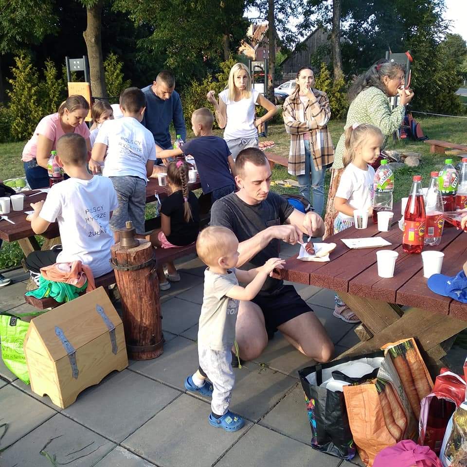 Osoby uczestniczące w pikniku, wspólnie jedzą posiłek.