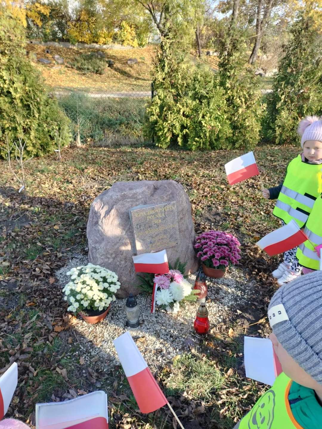 Pomnik z kwiatami i flagami Polski ustawionymi obok niego.