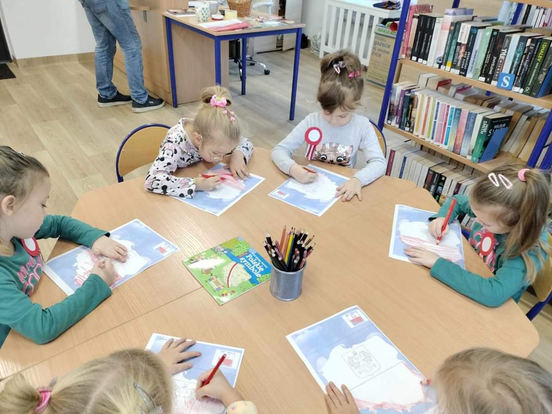 Grupa dzieci siedzących przy stole, przed nimi kartki z mapą Polski.