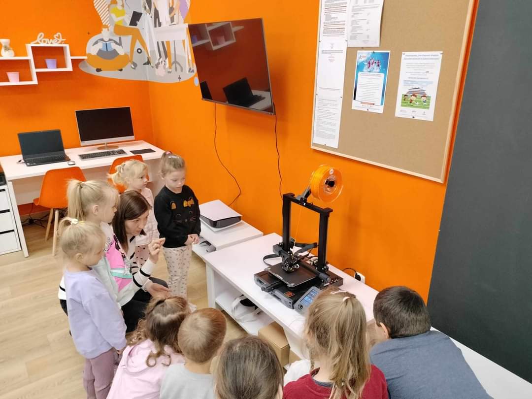 Grupa dzieci zapoznających się z drukarką 3D.