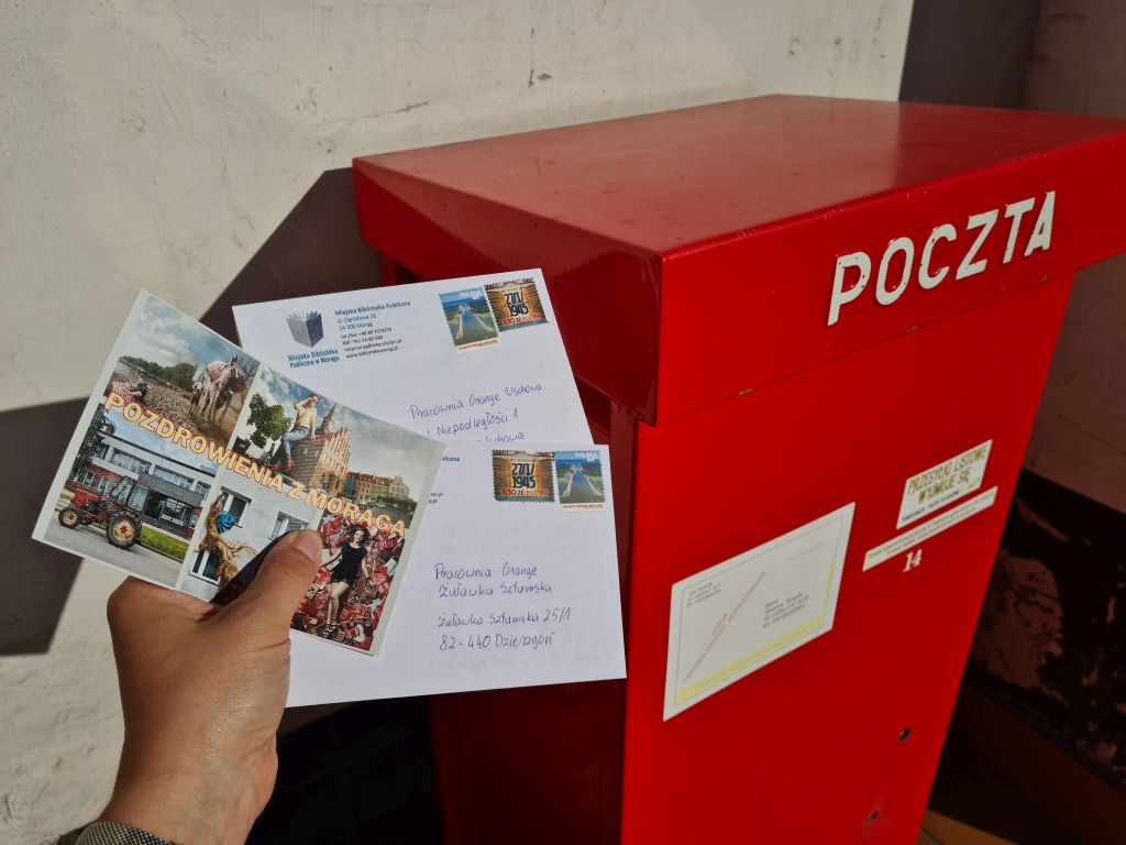 Dłoń z pocztówkami na tle skrzynki pocztowej