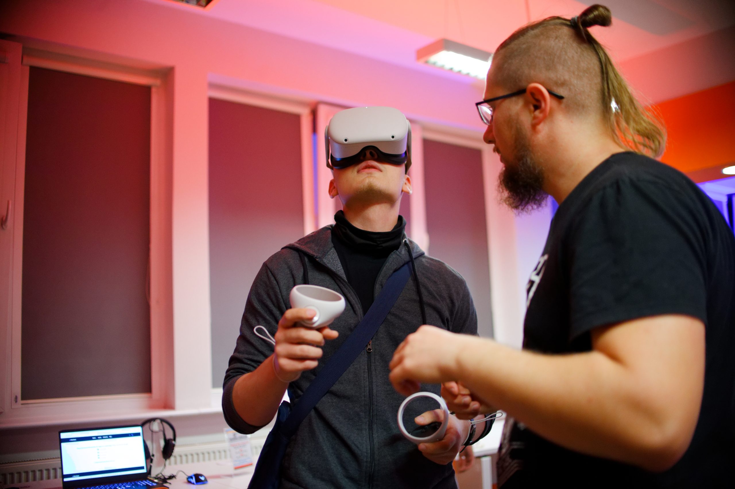 Dwóch mężczyzn - jeden korzysta z gogli VR, drugi stoi obok.