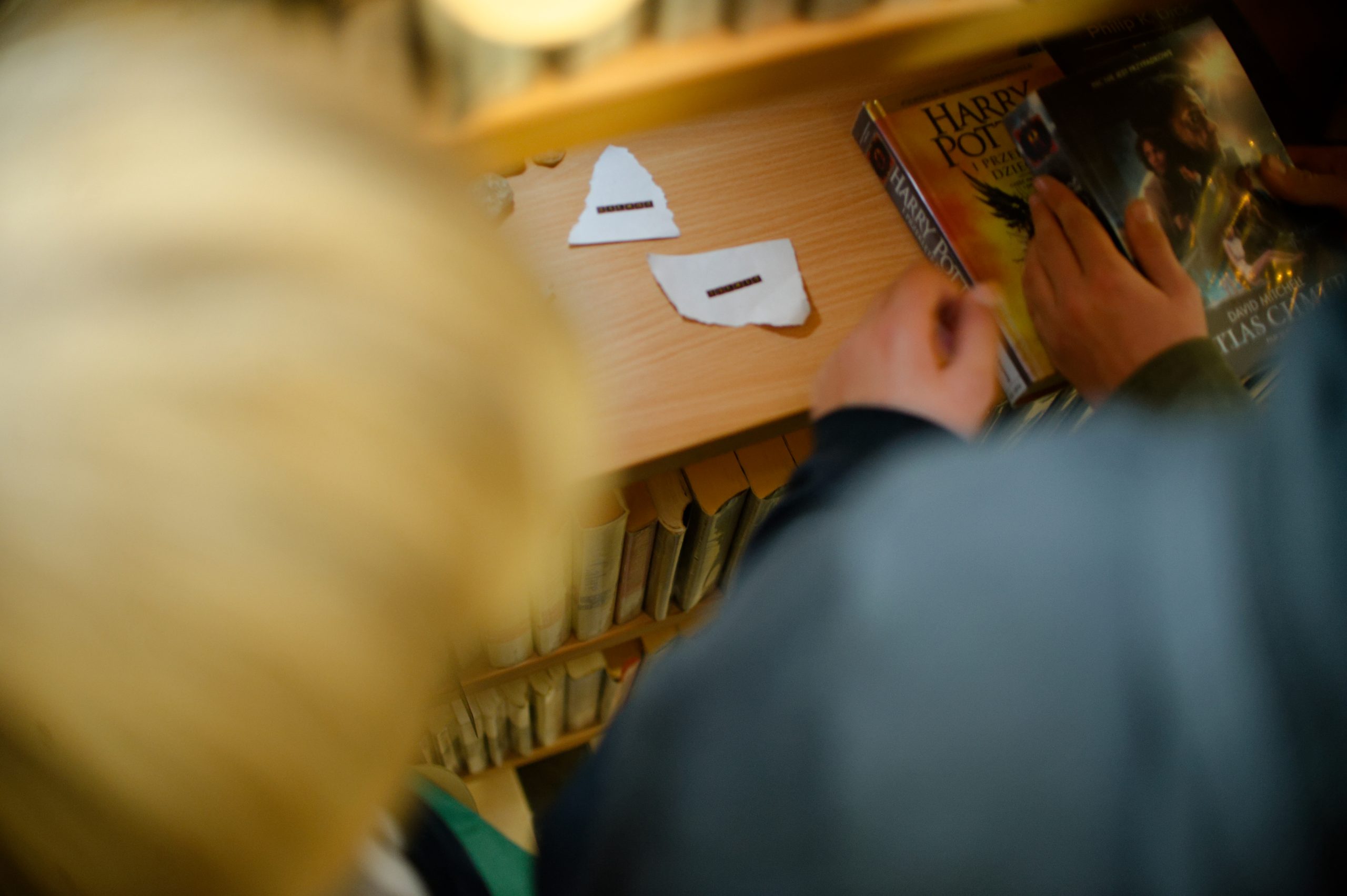 Widok na osoby patrzące na kawałki papieru z napisami leżącymi na bibliotecznej półce.