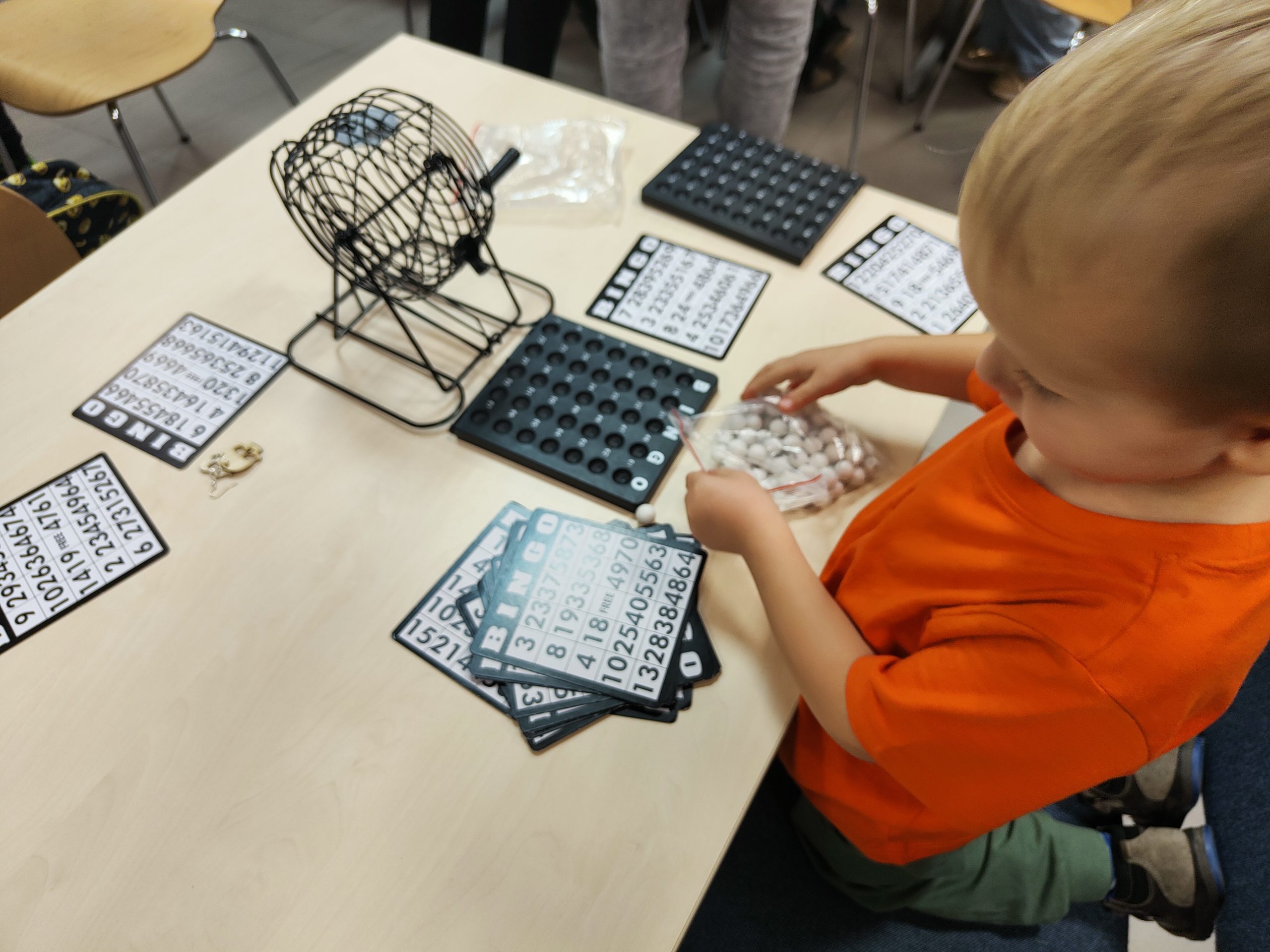 Dziecko układające na stole elementy gry w Bingo - karty, kulki i bębenek.