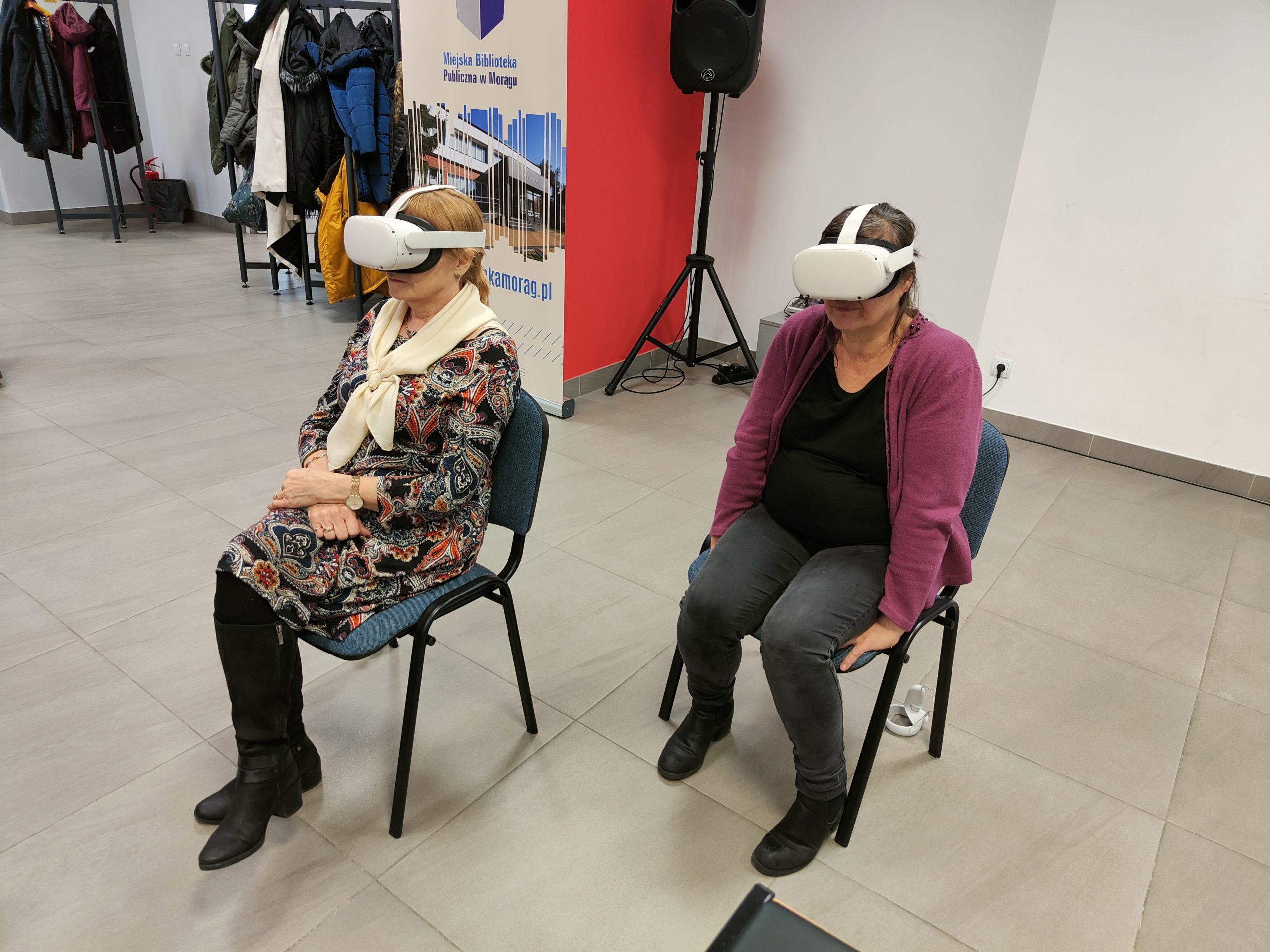 Dwie kobiety siedzą na krzesłach z założonymi na głowę goglami VR.