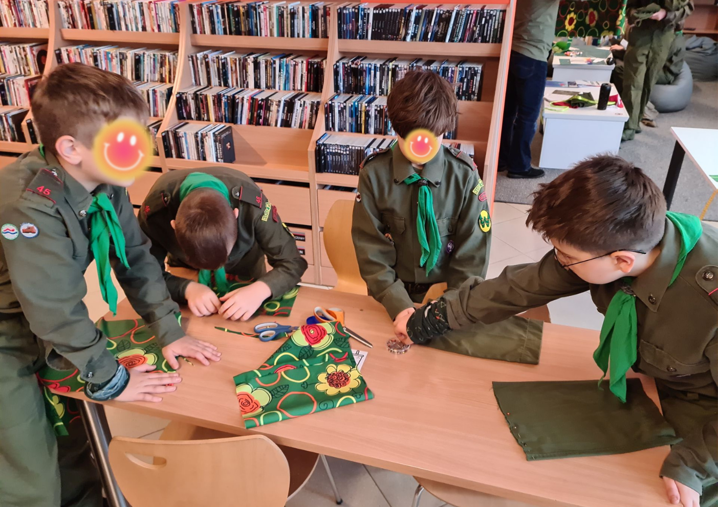 4 młodych chłopców w mundurach harcerskich spina szpilkami przy stole materiał do uszycia woreczków