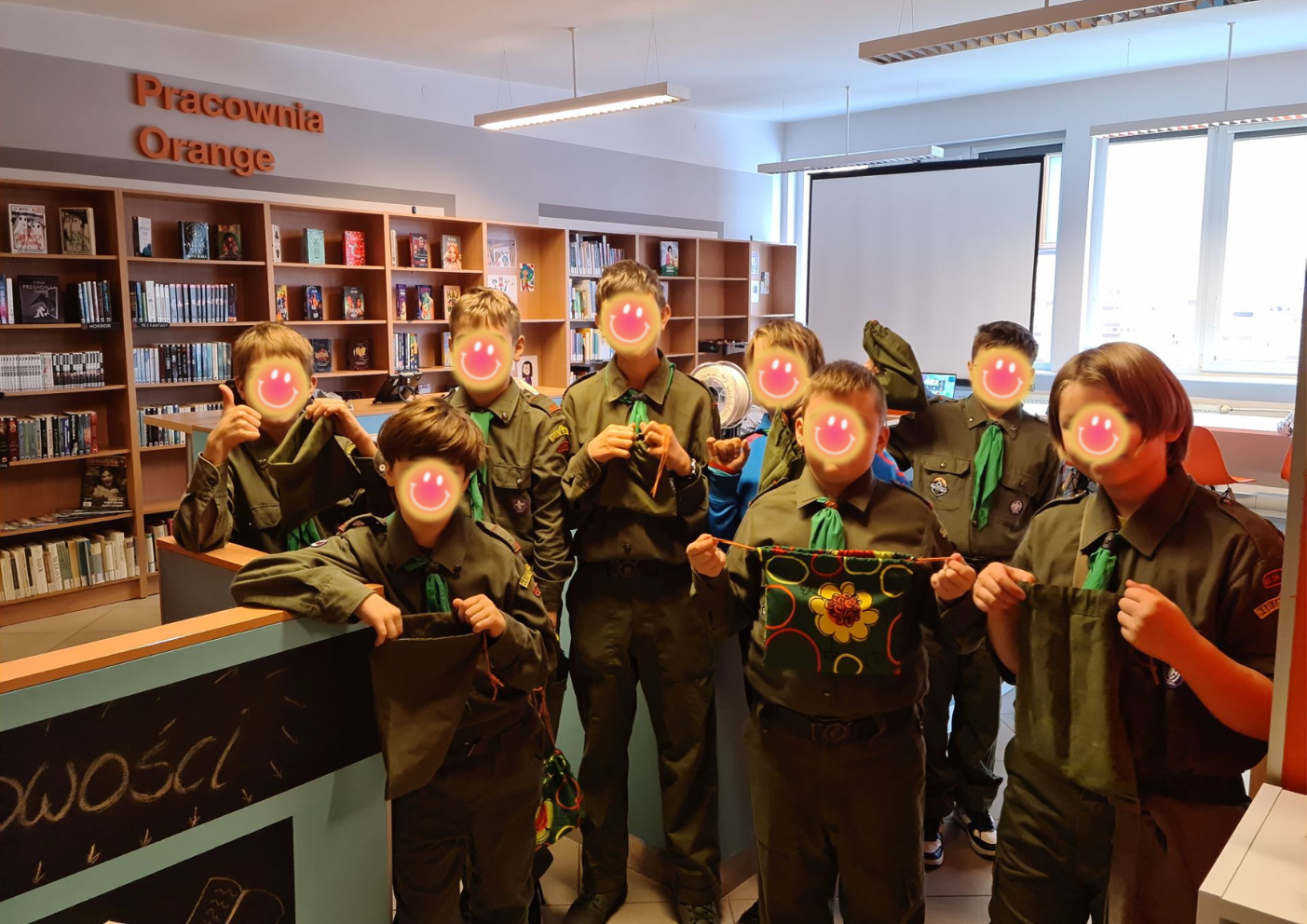 Grupa 8 młodych chłopców w mundurach harcerskich prezentuje uszyte przez siebie woreczki