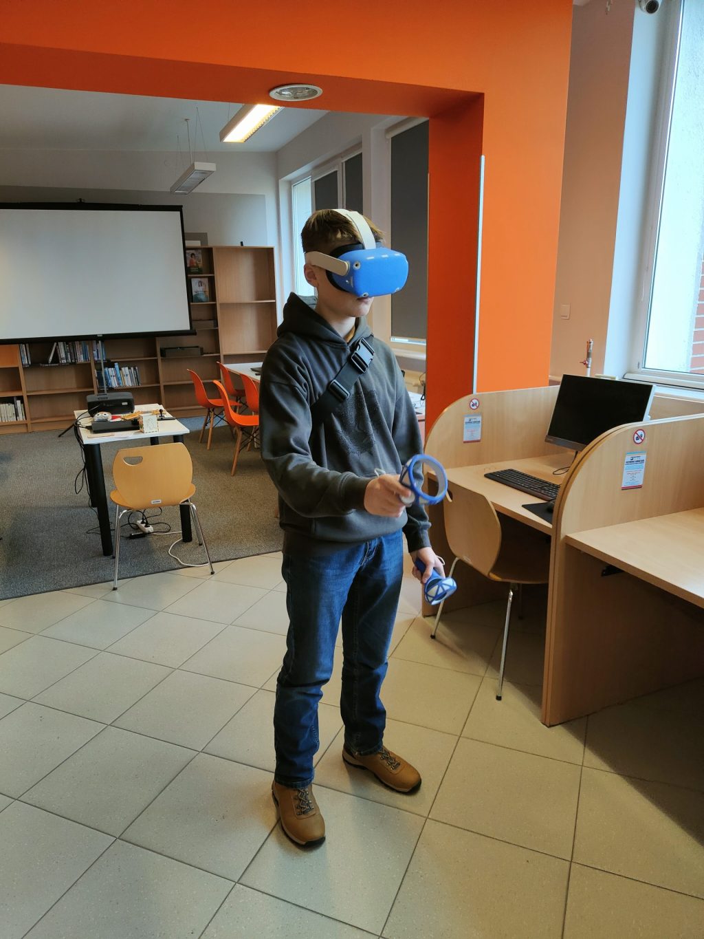 Chłopiec korzystający z gogli VR. W tle biurka i ekran projekcyjny.