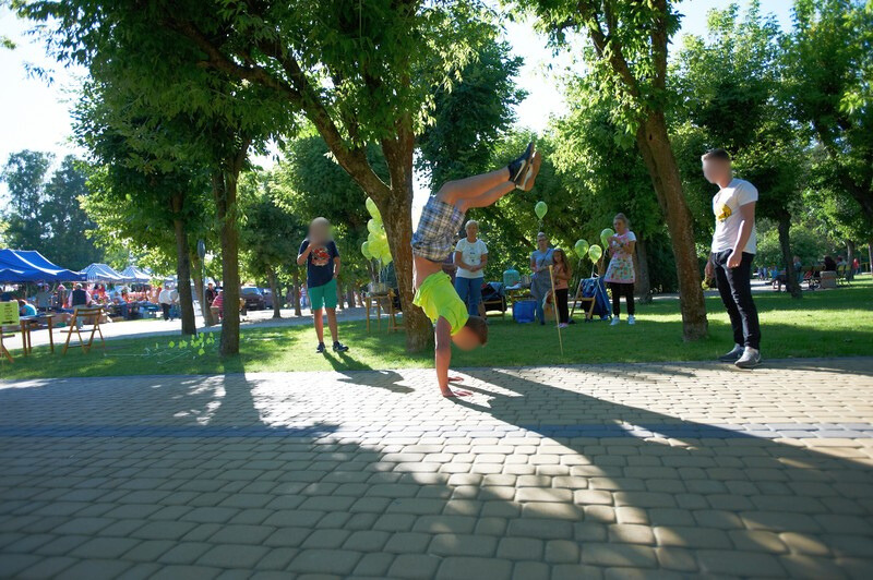 Gruma ludzi w parku, na pierwszym planie chłopak stoi na rękach