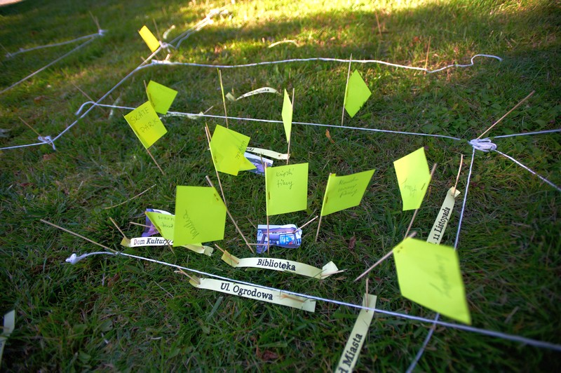 sznurki i karteczki wbite na patykach w trawę