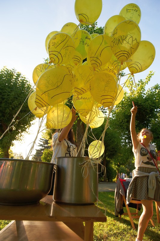 garnek z żółtymi, obok stoi dziewczyna i pokazuje na balon unoszącymi się balonami