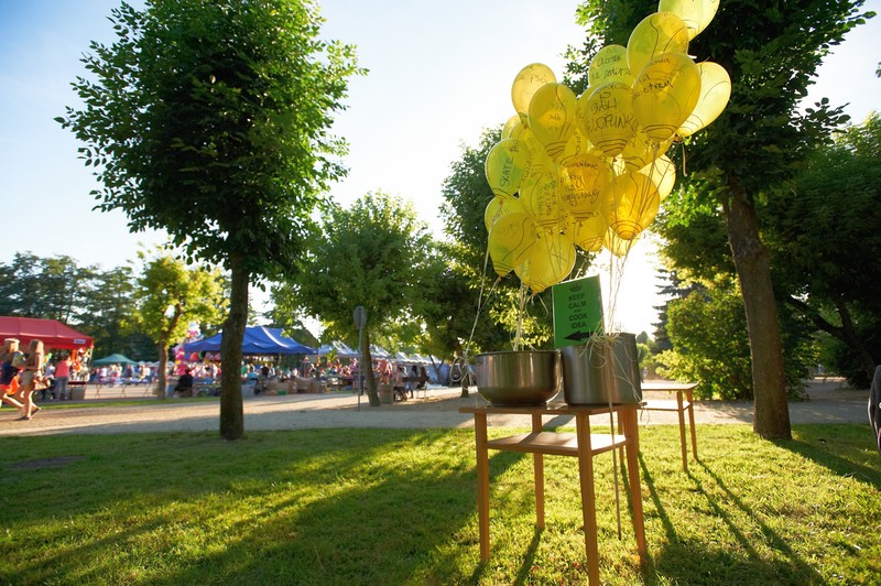 w parku stół z garnkiem i unoszącymi się żółtymi balonami