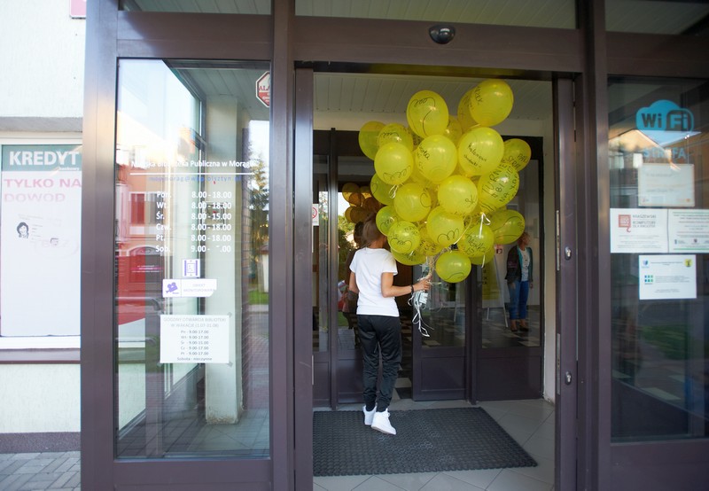 Dziewczyna wchodzi do budynku z pękiem unoszących się żółtych balonów