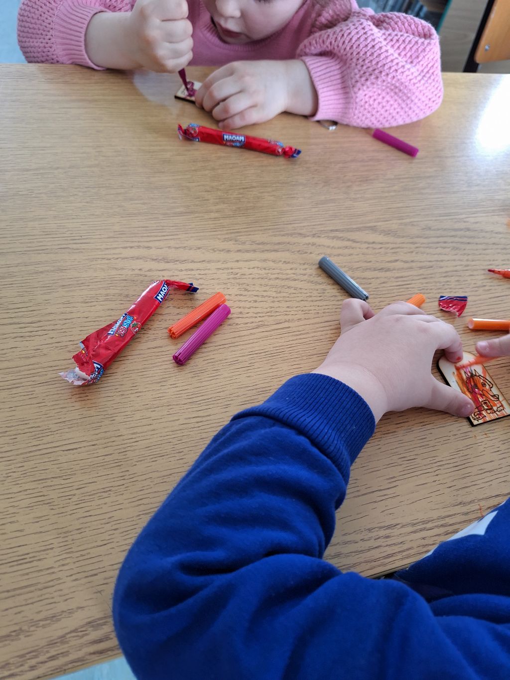 widok na ręce dzieci ozdabiających breloki ze sklejki