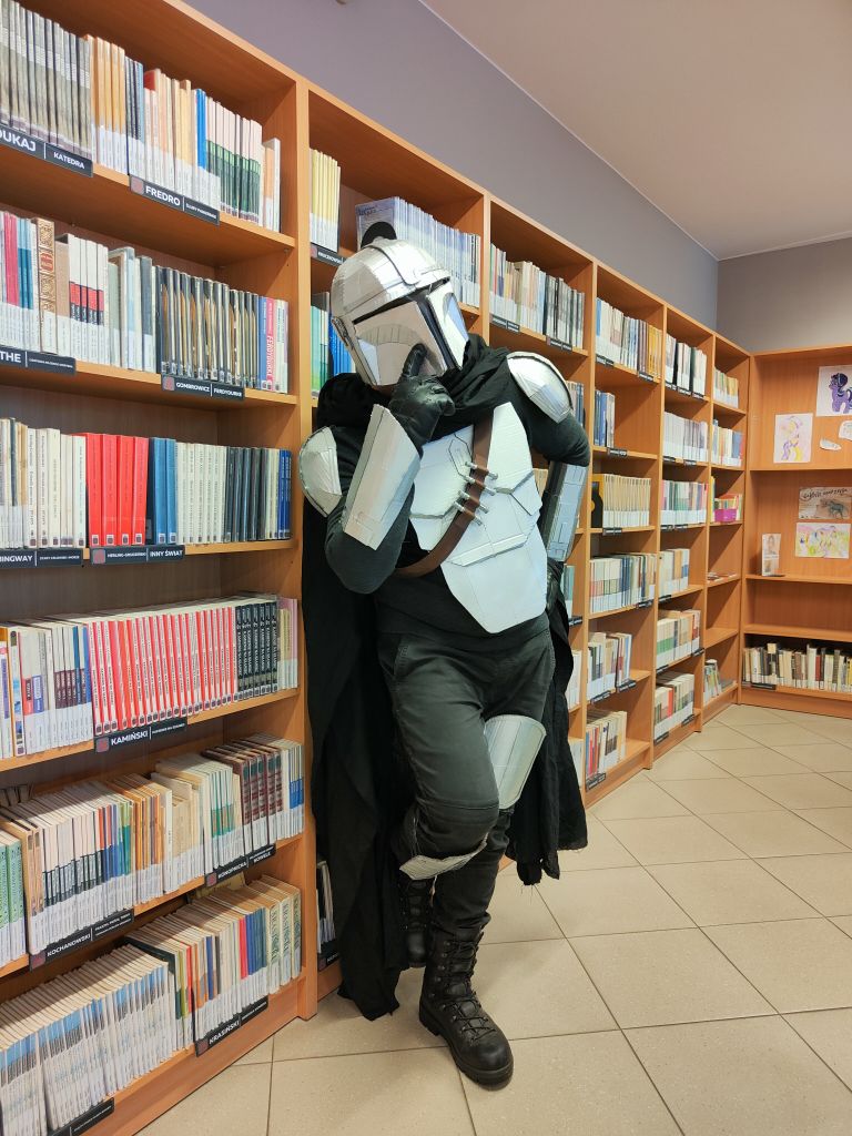 Człowiek w kostiumie postaci z Gwiezdnych Wojen pozuje na tle regałów z książkami