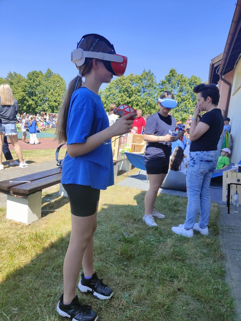 dwie dziewczynki korzystają z gogli wirtualnej rzeczywistości na dworze, obok jednej z nich stoi kobieta